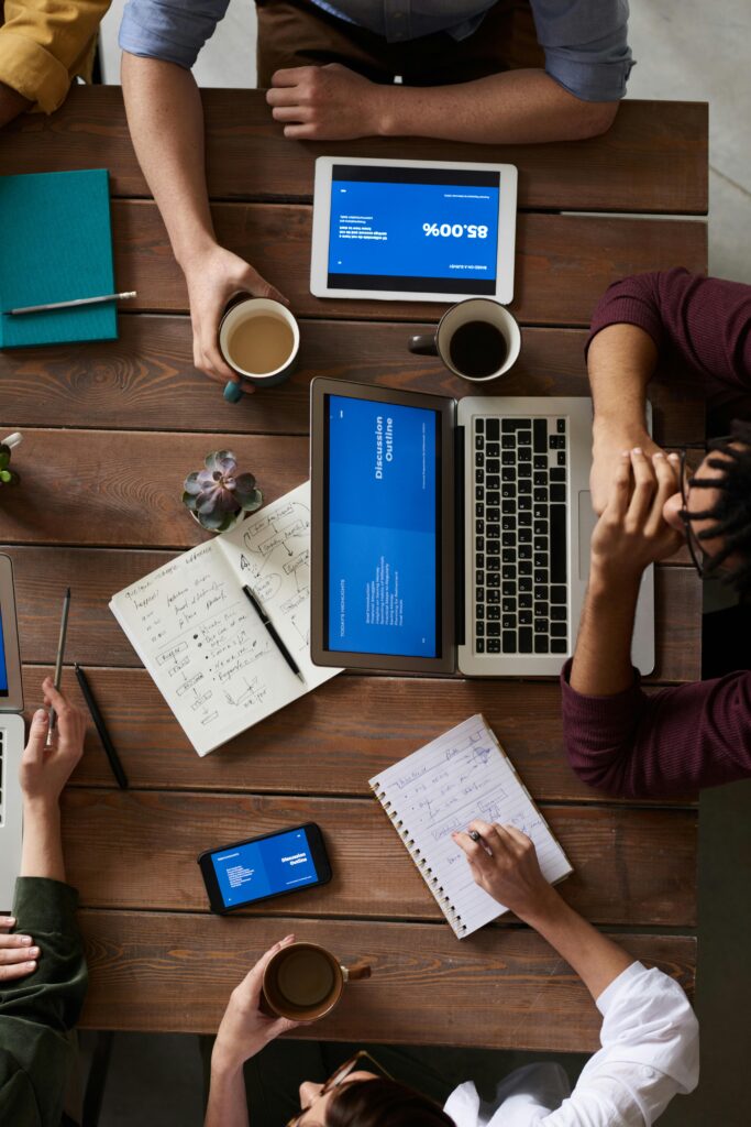 Group of coworkers discussing business strategies with laptops and tablets in a modern office setting.